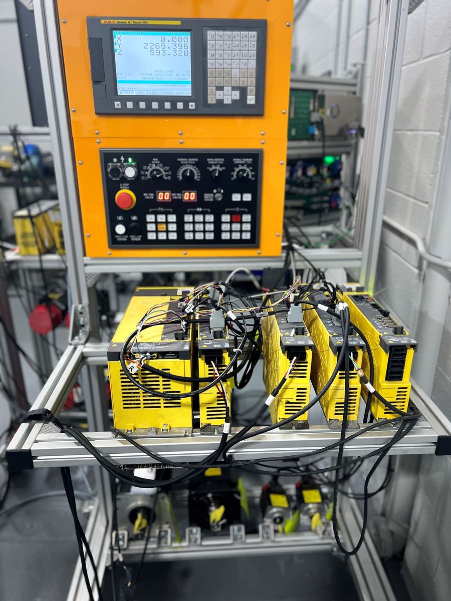 FANUC Series 0i-MD CNC control and a row of FANUC servo and spindle amplifiers wired to test motors on an AST test bench