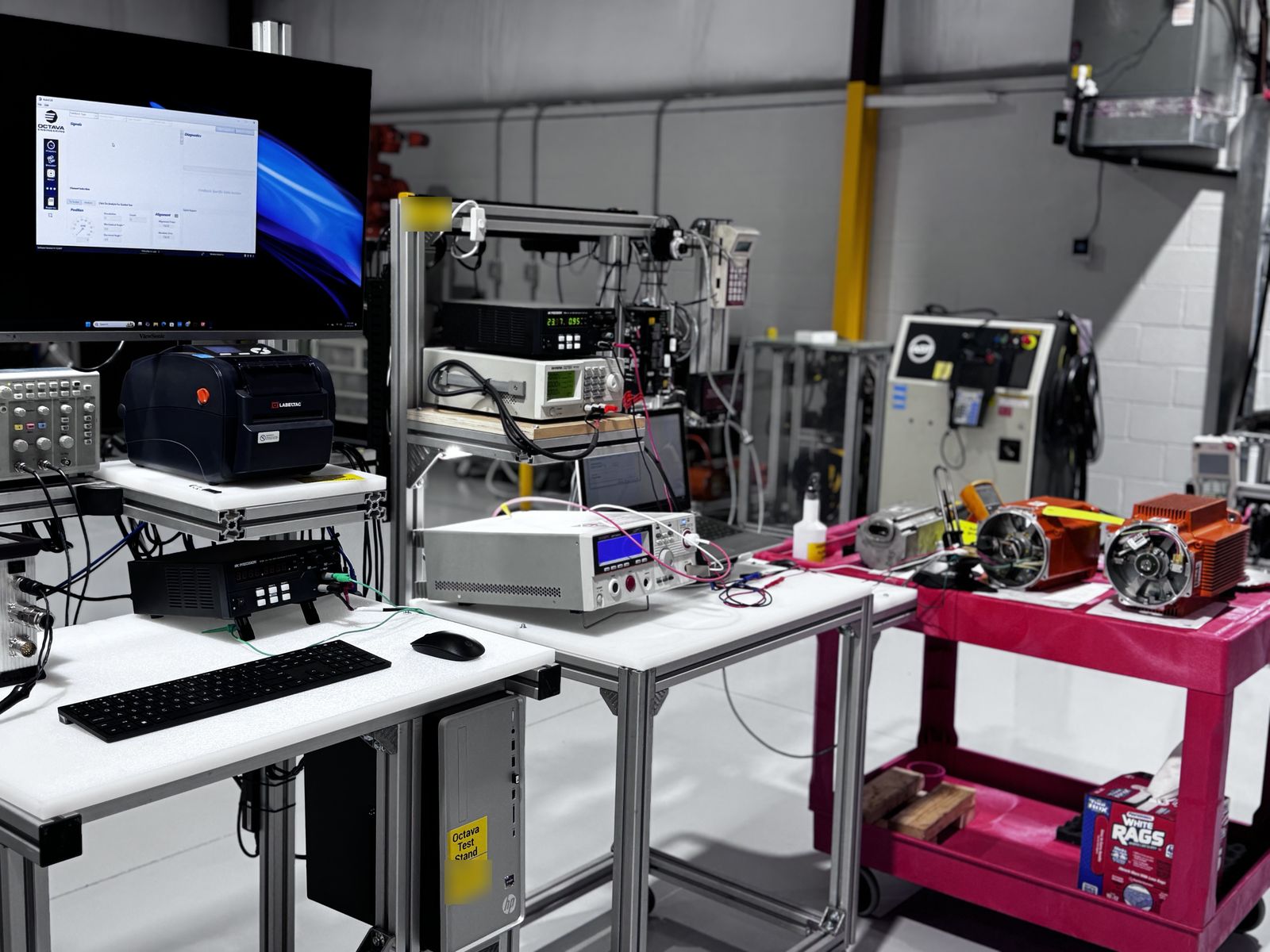 AST servo motor test lab with test instruments, power supplies, an Octava encoder test stand and servo motors on a cart awaiting testing