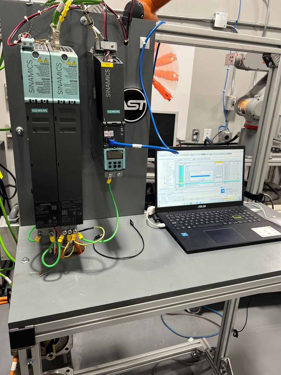 Siemens SINAMICS line and motor modules with a control unit, connected to a laptop running commissioning software on an AST test bench